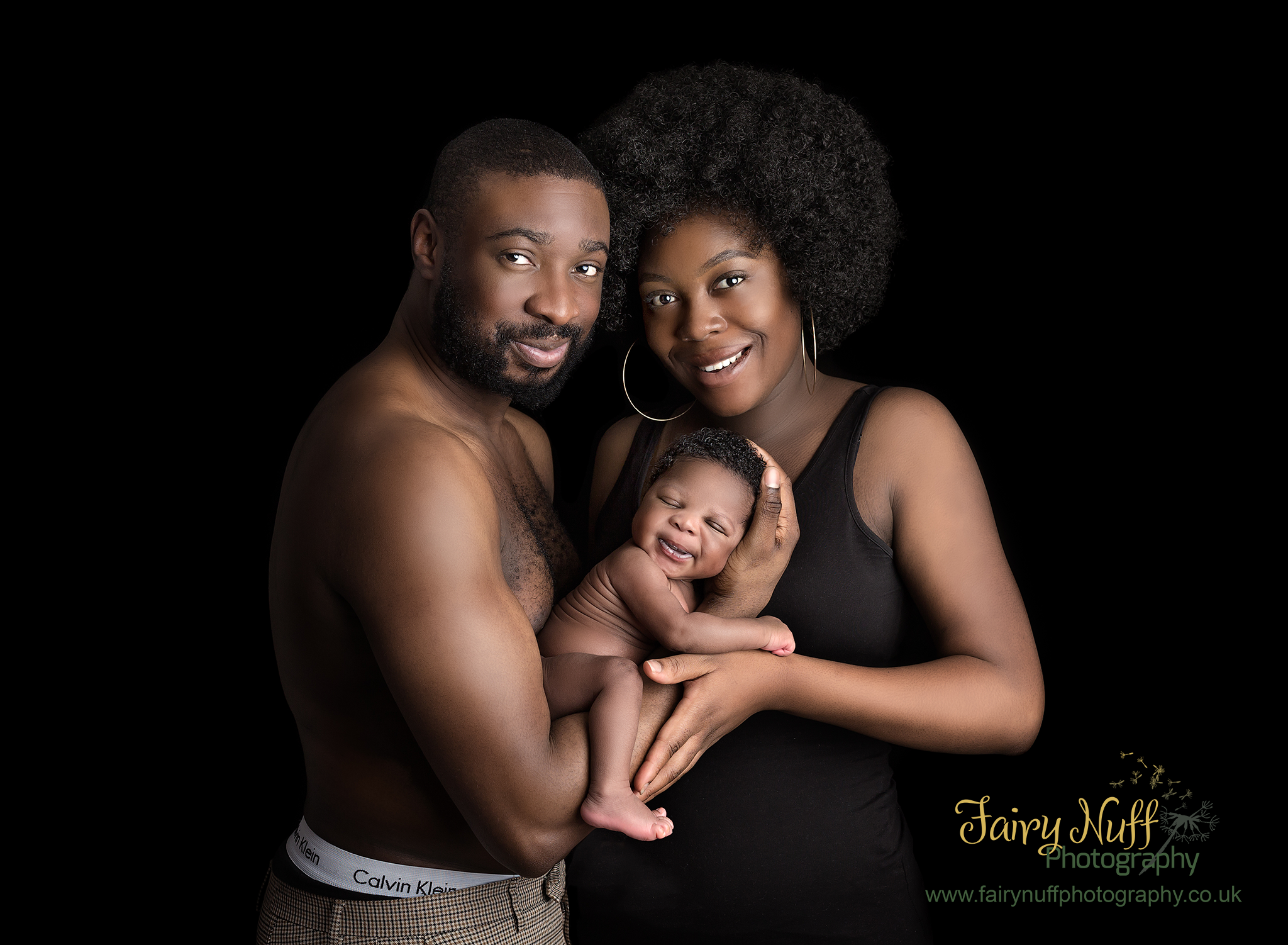 Mu and Dad holding a smiling newborn baby in their arms, facing eachother against a black background. Newborn photoshoot at Fairy Nuff Photography, Nottingham