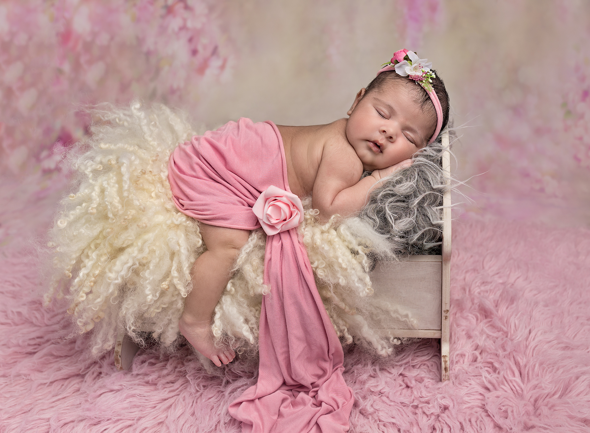 Newborn baby girl fast asleep on a bed prop with a pink floral backgrounf at a newborn baby photoshoot at Fairy Nuff Photography, Nottingham. 