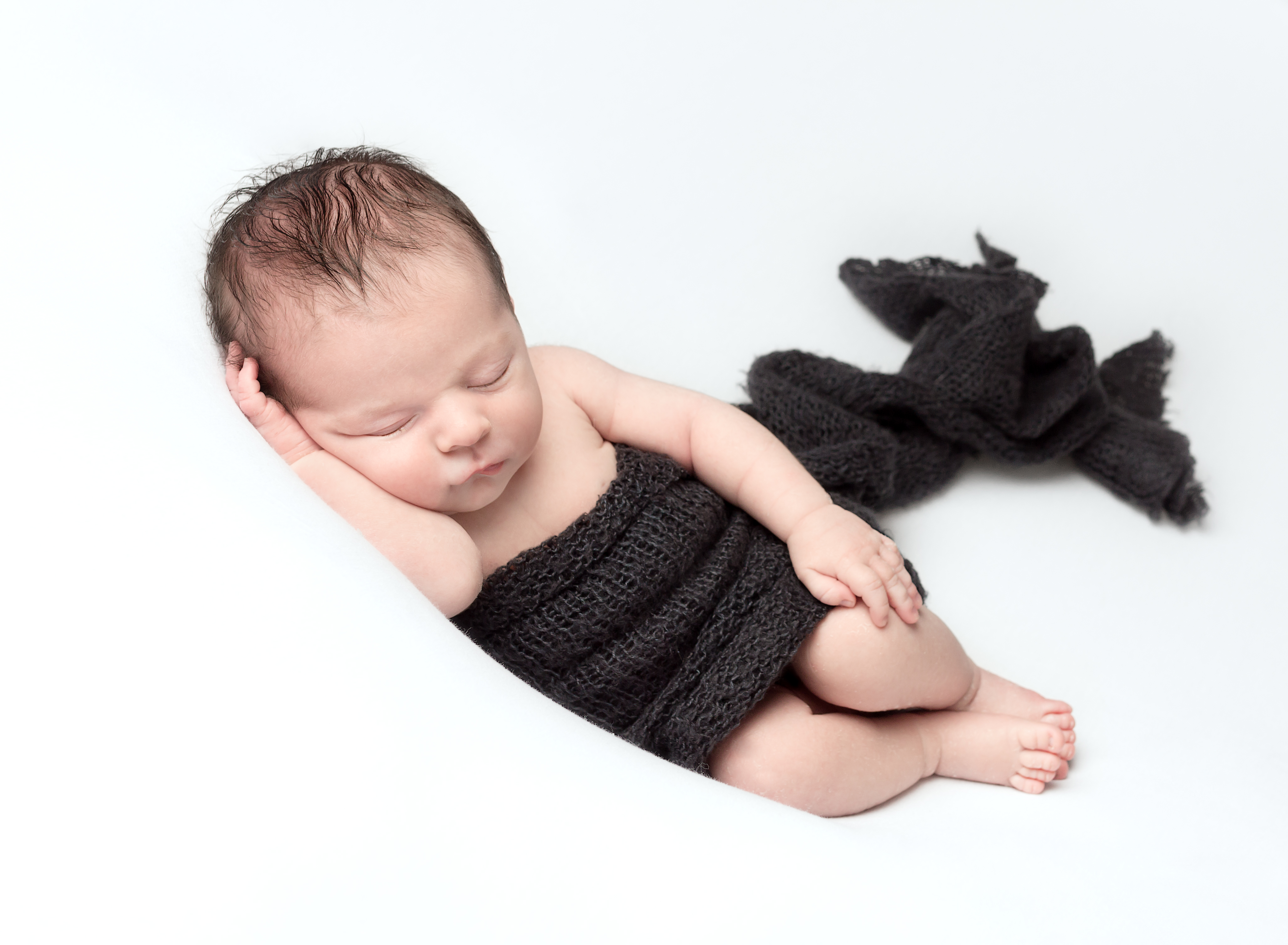 Newborn baby, sleeping peacefully on his side with a dark blue wrap at a newborn baby photoshoot at Fairy Nuff Photography, Nottingham. 