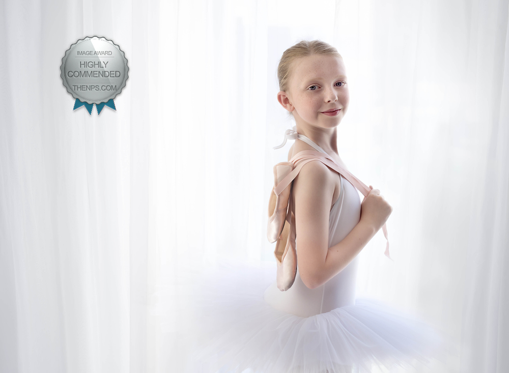 Award winning image of a young girl in ballet tutu holding a pair of ballet shoes over her shoulder