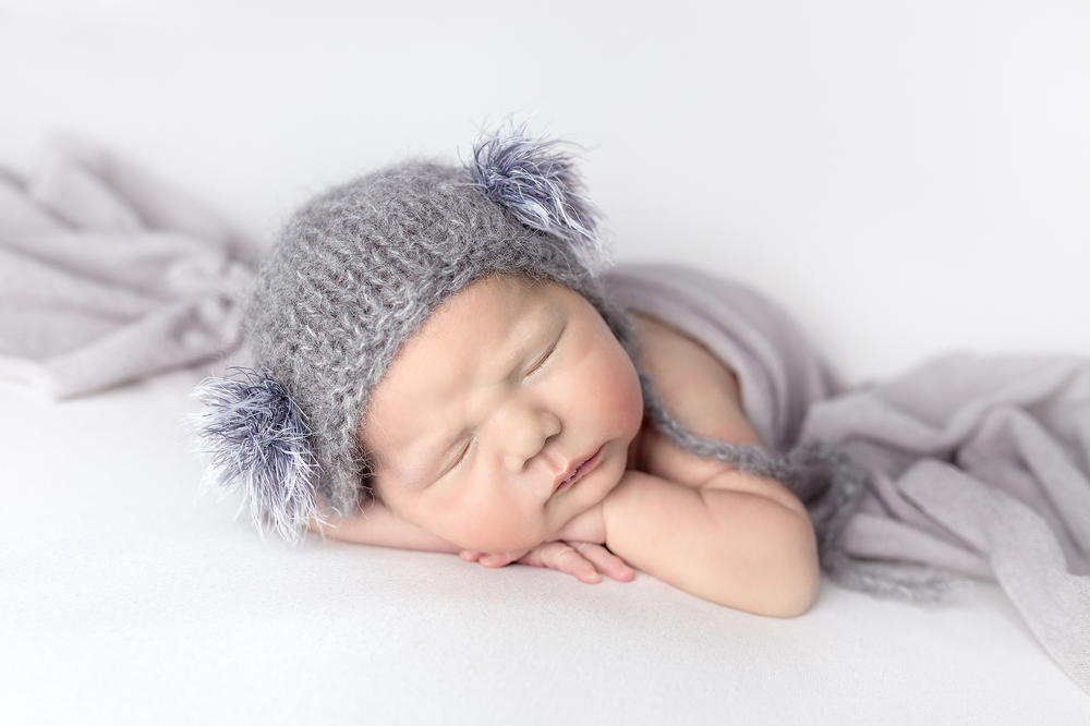 Newborn baby posed in head on hands with grey wrap and hat