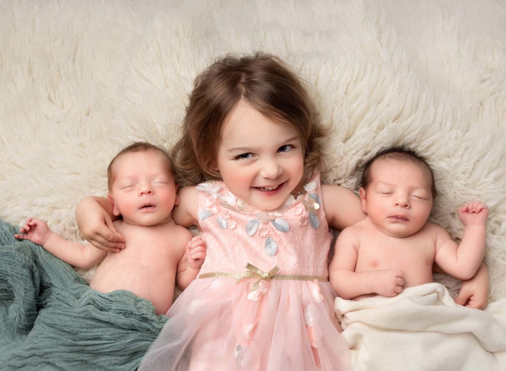 Young girl on her back with her twin baby brother posed on either side of her at a newborn twin photo shoot