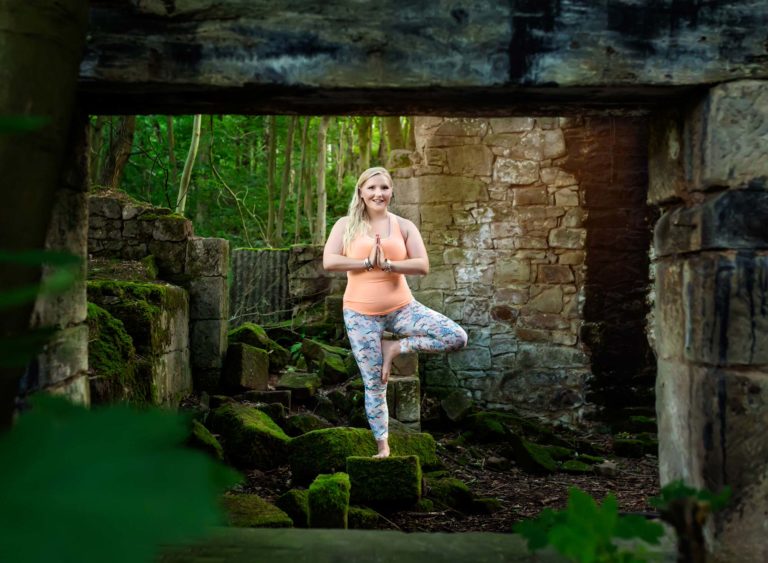 Yoga teacher in tree pose in an outdoor forest setting at a business photography session