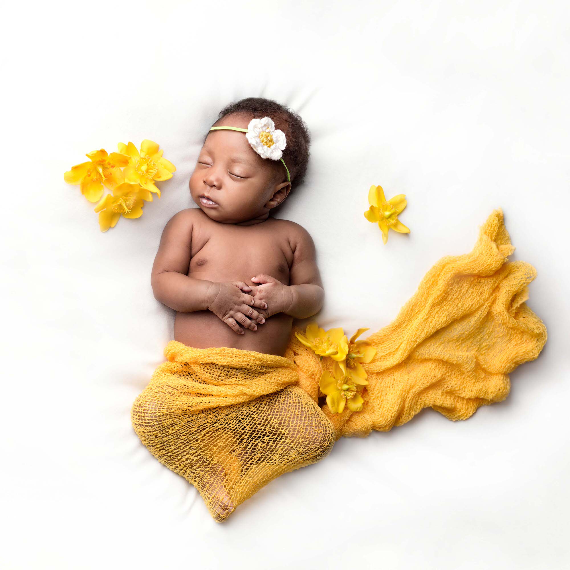 Newborn baby posed on her back, surrounded by yellow flowers