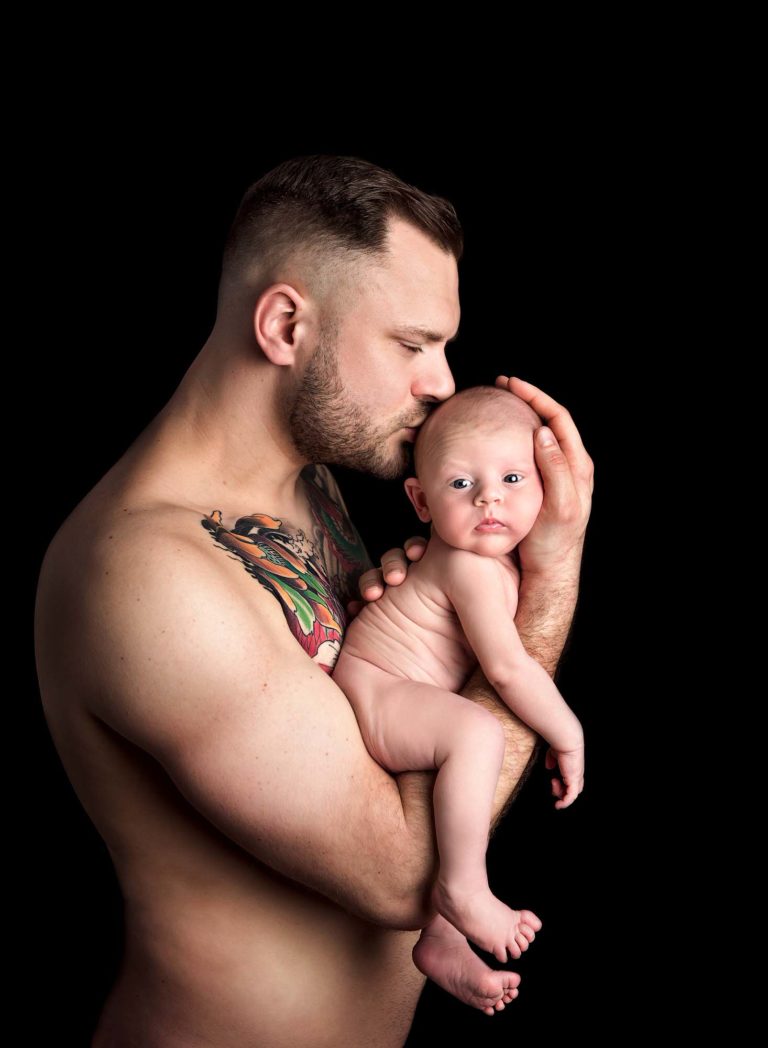 Dad holding his newborn in his arms and kissing his head at a baby photoshoot