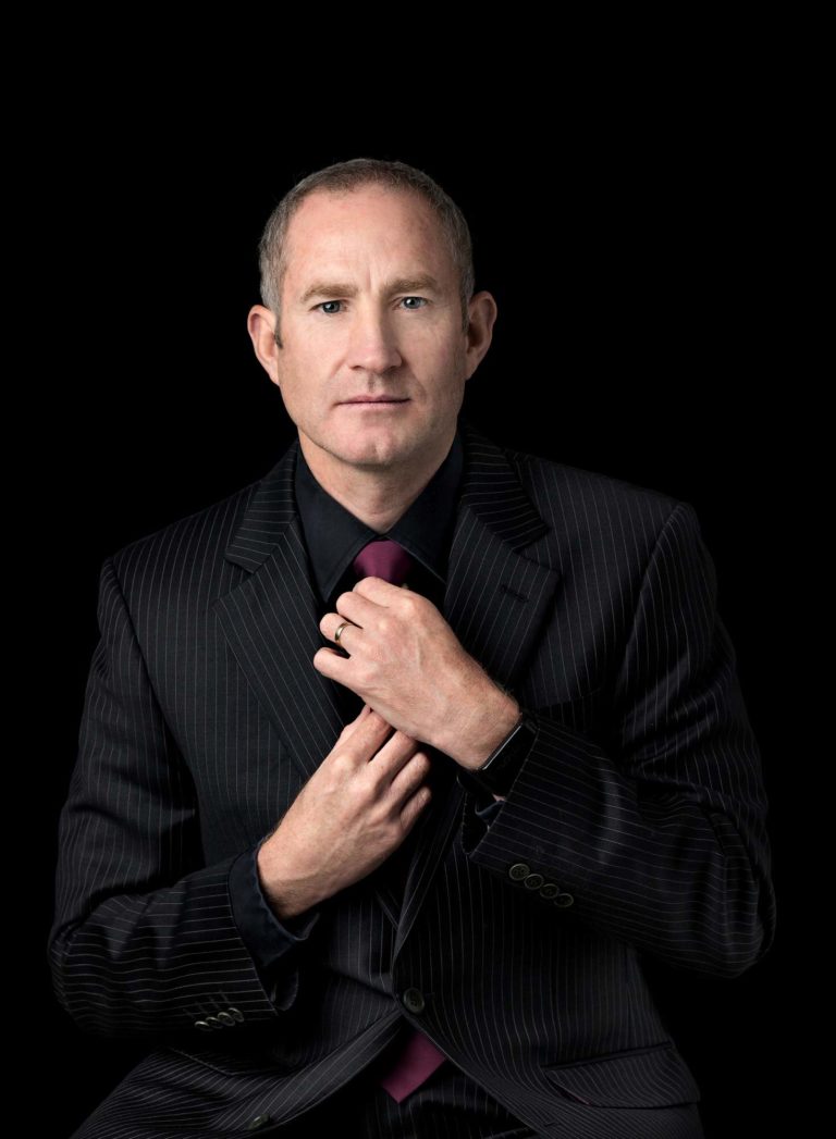 Business man in a suit arranging his tie against a black backdrop at a business headshot photography session