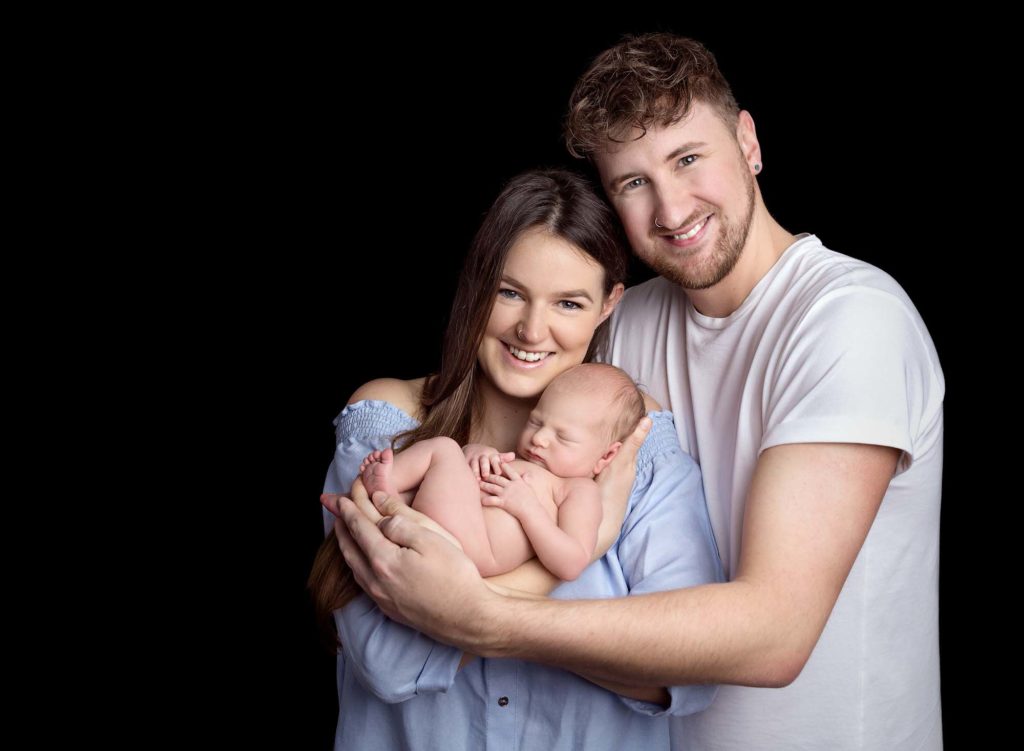 Smiling parents holding their newborn baby together at a baby photoshoot