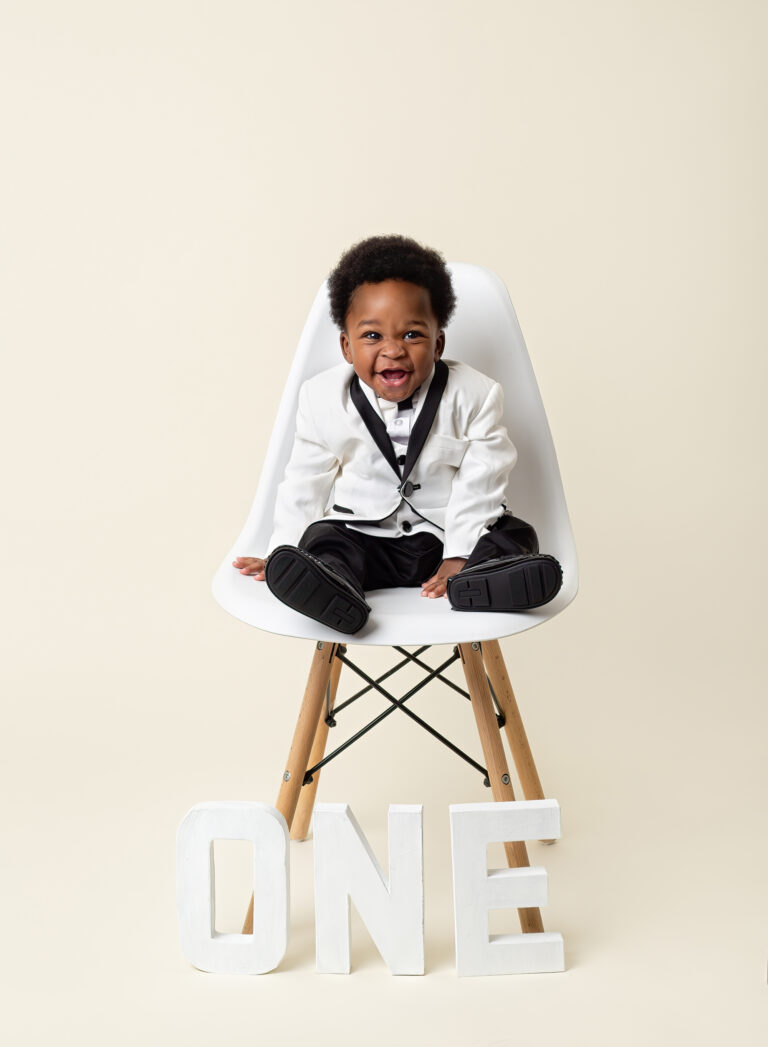 First Birthday portrait section, one year old boy in a white tuxedo laughing on a white chair. James Bond Theme 1st Birthday photography session, Fairy Nuff Photography, Nottingham