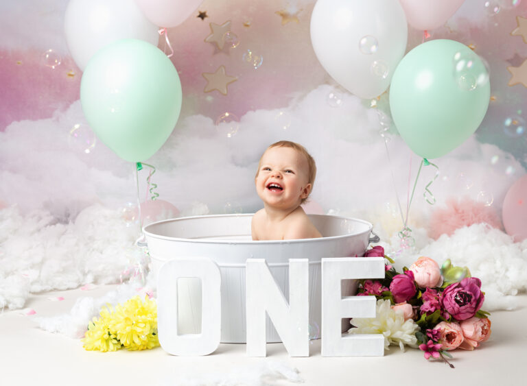Splish splash bubble bath section of 1st Birthday photography session. One year old girl in bath with pink and green balloons and a cloud backdrop. 1st Birthday photography session, Fairy Nuff Photography, Nottingham