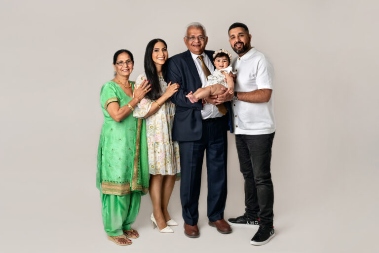 A family group including a baby, parents and grandparents against a cream backdrop at a studio photography session at Fairy Muff Photography, Nottingham