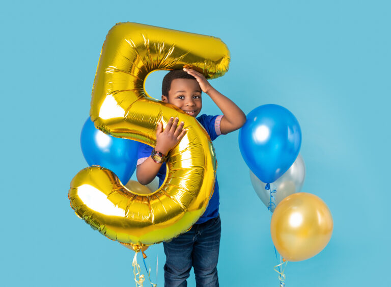 5th Birthday photoshoot of a boy holding a gold number 5 balloon on a blue backdrop. Fairy Nuff Photography, Nottingham