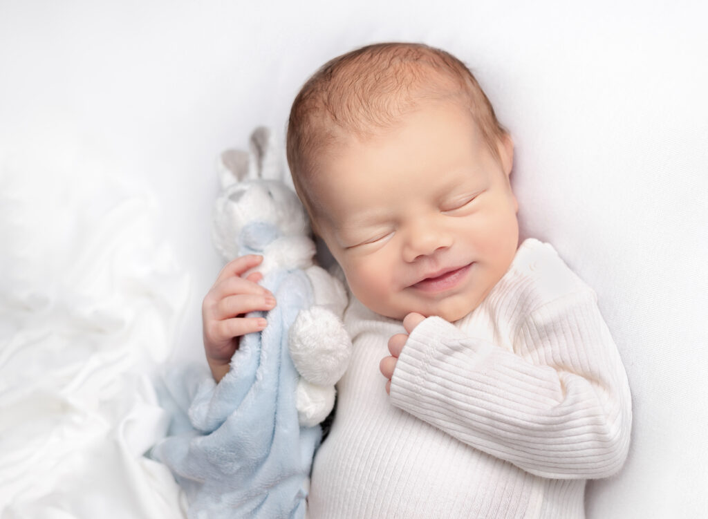 Newborn baby smiling and cuddling a teddy at Fairy Nuff Photography, Nottingham - newborn baby photography specialist.