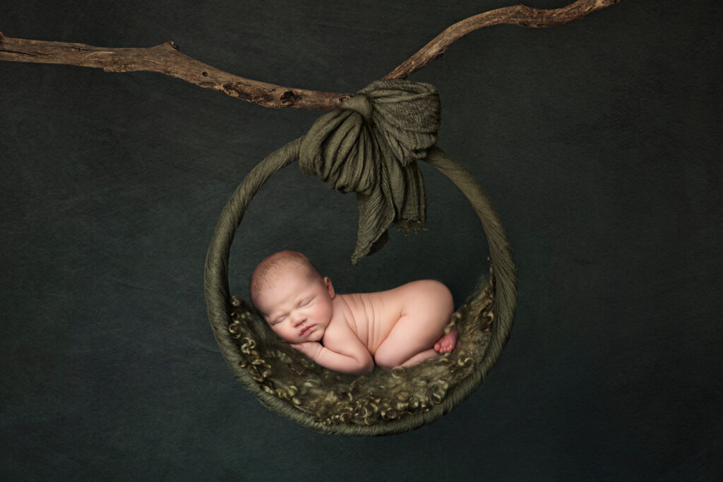 Newborn baby boy sleeping peacefully and digitally composited into a green background and rustic swing, by Fairy Nuff Photography, Nottingham